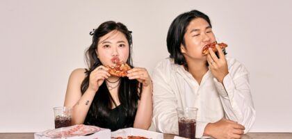 A couple savoring pizza and cola, sitting indoors with takeaway boxes.