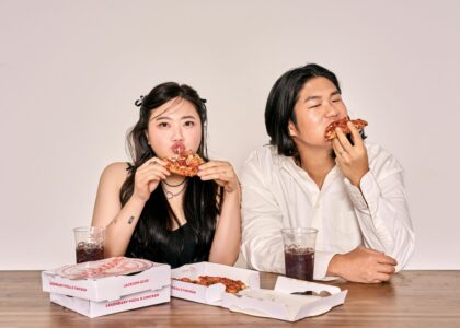A couple savoring pizza and cola, sitting indoors with takeaway boxes.