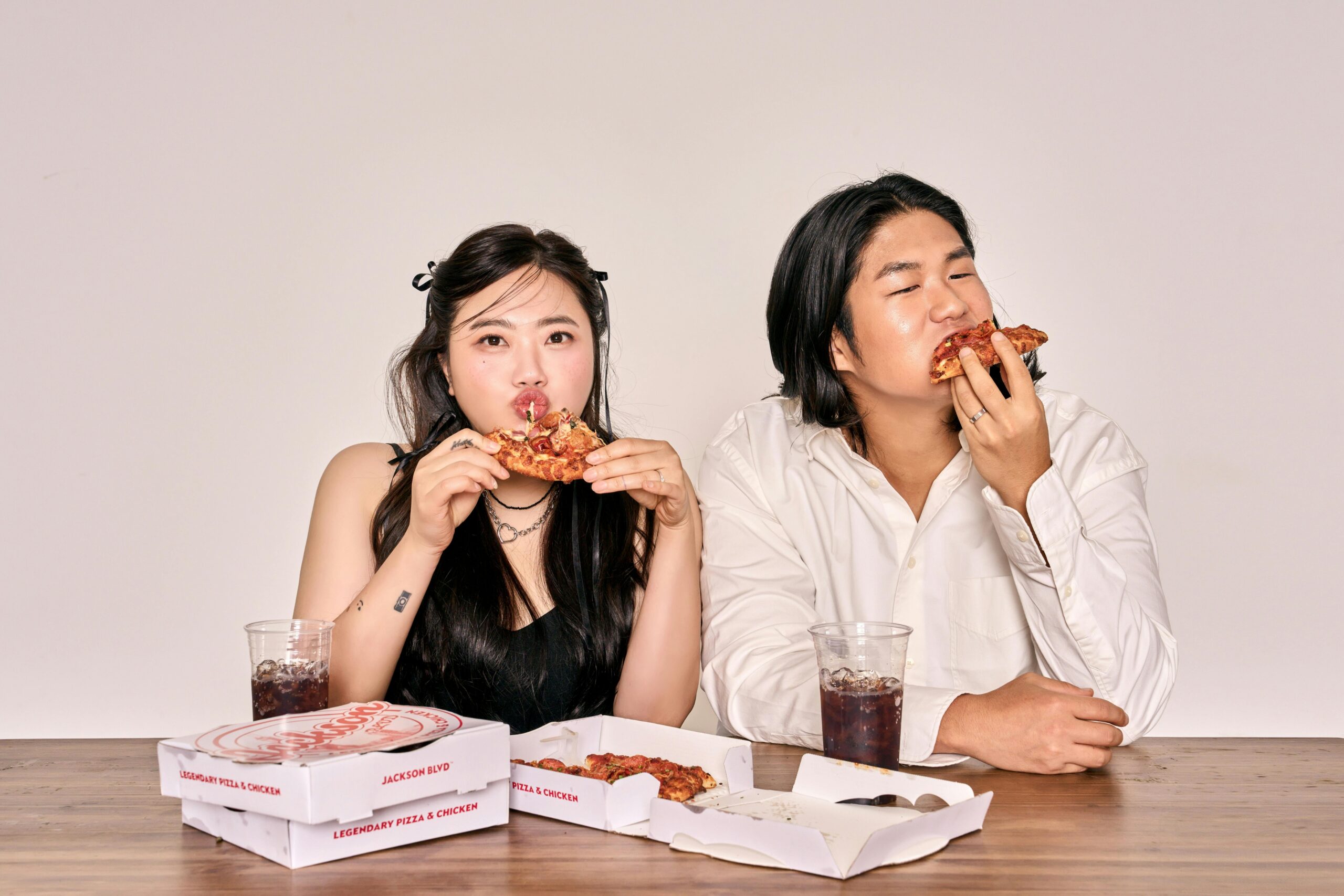 A couple savoring pizza and cola, sitting indoors with takeaway boxes.