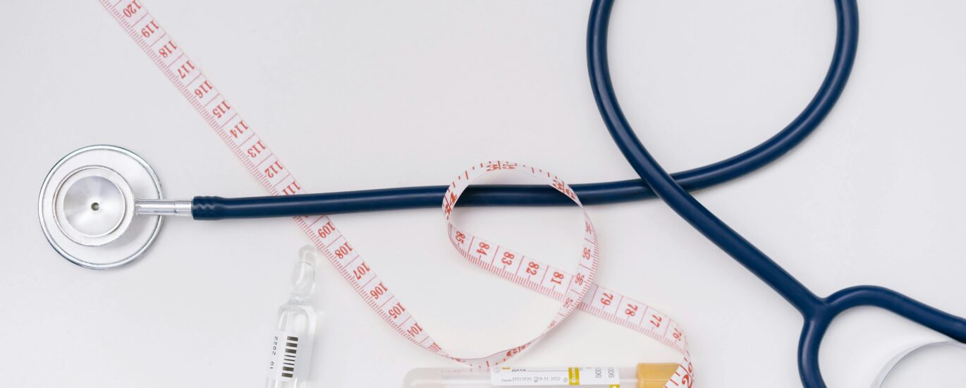 A stethoscope, ampoule, and tape measure on a white background symbolize healthcare essentials.